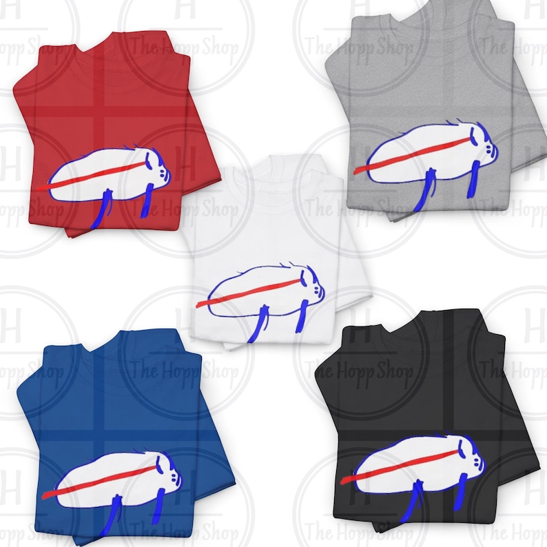 Pu&ograve; includere: Cinque magliette a maniche corte in rosso, grigio, bianco, blu e nero. Ogni maglietta presenta una grafica centrale di una creatura bianca di forma ovale con una linea rossa orizzontale e due linee blu verticali sul corpo.