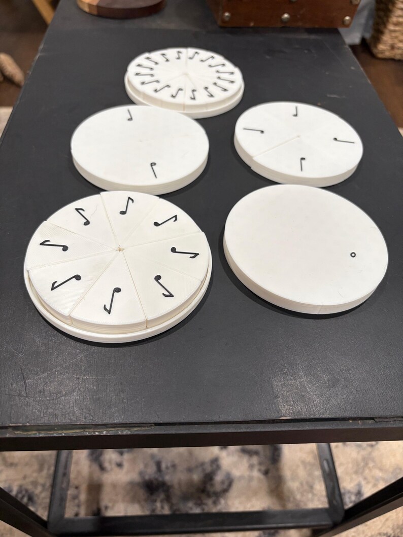May include: A collection of white, circular objects with black markings, including musical notes and lines. Some are segmented, and others are solid. The objects are arranged on a dark surface, suggesting a game or educational tool.