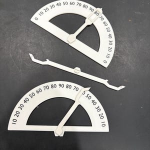 May include: Two white plastic protractors with a movable arm. The protractors are marked with numbers from 0 to 90 degrees.