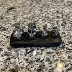 May include: A black plastic socket organizer with four silver sockets of different sizes.