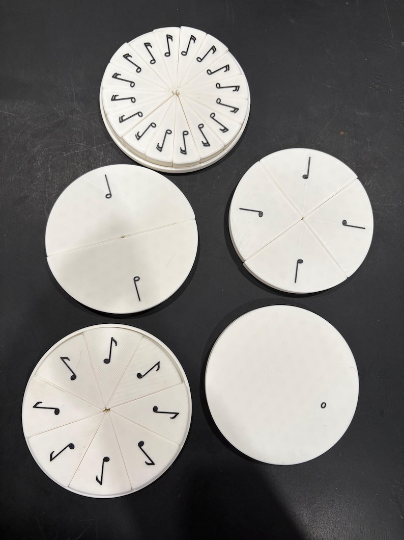 May include: A collection of white, circular music-themed educational toys. Some have black musical notes around the edges, while others are divided into segments with single notes. The toys are arranged on a dark surface.