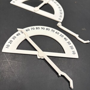 K&ouml;nnte beinhalten: Zwei wei&szlig;e Kunststoff-Geodreiecke mit schwarzen Markierungen. Die Geodreiecke sind in Grad von 0 bis 90 gekennzeichnet. Die Geodreiecke sind zum Messen von Winkeln bestimmt.