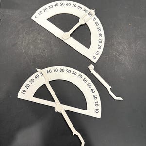 K&ouml;nnte beinhalten: Zwei wei&szlig;e Kunststoff-Geodreiecke mit schwarzen Markierungen. Die Geodreiecke sind in Grad von 0 bis 90 gekennzeichnet. Die Geodreiecke werden zum Messen von Winkeln verwendet.