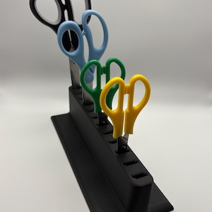 May include: A black scissor holder with four pairs of scissors. The scissors have black, blue, green, and yellow handles. The holder is rectangular with slots for each pair of scissors.