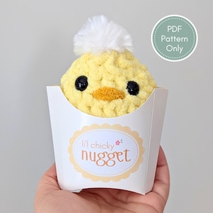 May include: A yellow crocheted chick with black eyes and an orange beak, topped with a white pom-pom, sits in a white paper container. The container has a label that reads "lil' chicky nugget". A circular graphic indicates "PDF Pattern Only".