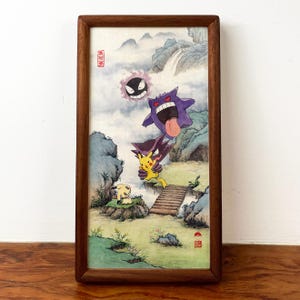 Puede incluir: Pintura a la acuarela enmarcada con personajes de Pokémon en un paisaje con montañas, cascadas y un puente de madera. El marco es de madera marrón oscuro. La pintura incluye un Gastly, Gengar, Haunter, Pikachu y una pequeña criatura blanca parecida a un perro.