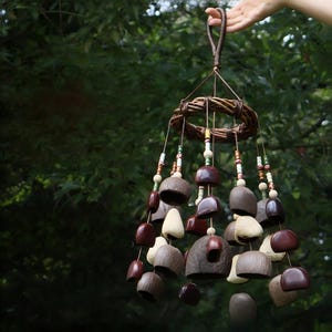 Può includere: Un carillon fatto a mano con una cornice circolare intrecciata e perline sospese. Il carillon ha varie campane e perline marroni, beige e crema. Il carillon è sospeso da un cordoncino intrecciato marrone.