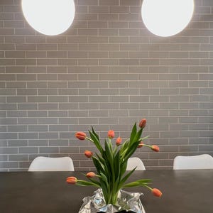 May include: A bouquet of orange tulips with green stems and leaves arranged in a crinkled silver metallic foil base. The flowers are positioned on a dark surface, with the stems gathered together at the center of the reflective silver material.