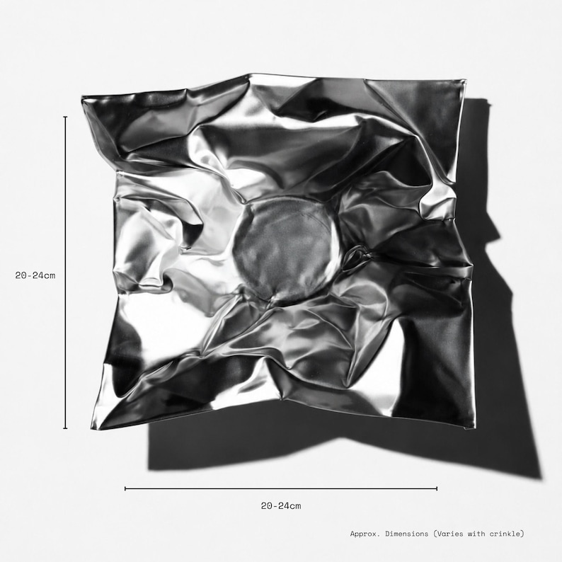 May include: A square, metallic silver bowl with a highly reflective, crinkled surface texture. The bowl features a central circular depression and irregular folds throughout. Text indicates dimensions of 20-24 cm, noting they vary with the crinkle.