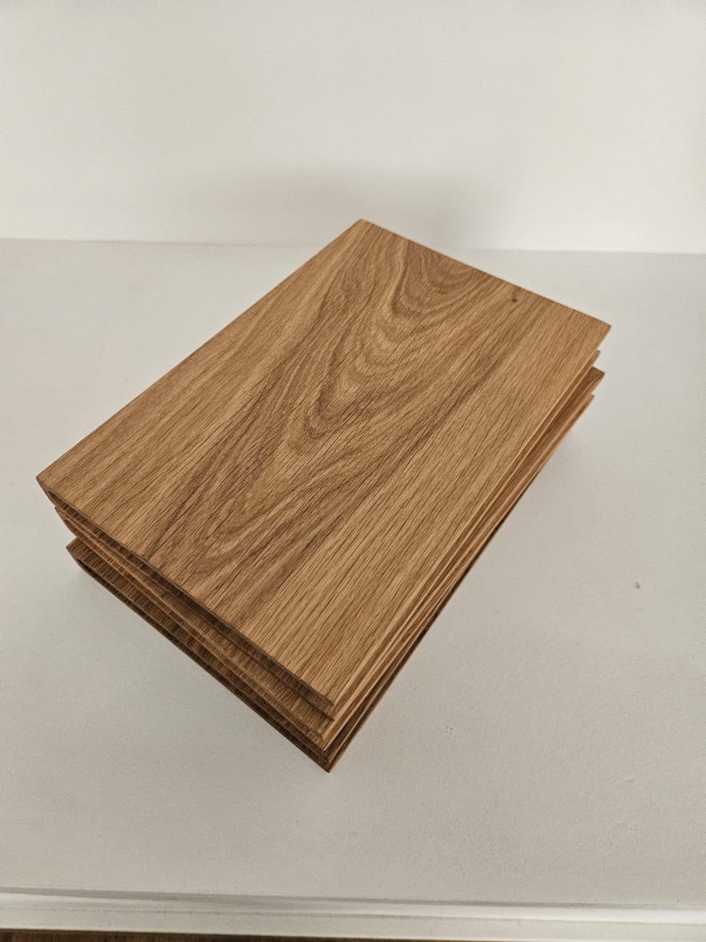 May include: A stack of four rectangular wooden planks. The planks are a light brown color with visible wood grain patterns. The edges of the planks are also visible, showing the layered construction of the wood.