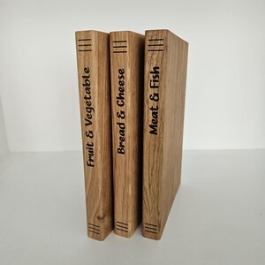 May include: Three wooden cutting boards with the labels "Fruit & Vegetable", "Bread & Cheese", and "Meat & Fish" in black text. Each board has three parallel lines etched at the top and bottom. The boards are made of light brown wood.