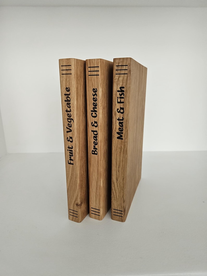 May include: Three wooden cutting boards with the labels "Fruit & Vegetable", "Bread & Cheese", and "Meat & Fish" in black text. Each board has three parallel lines etched at the top and bottom. The boards are made of light brown wood.