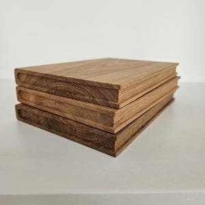 May include: Three stacked wooden blocks with a book-like appearance. The blocks are made of light brown wood, with visible grain patterns. The edges are slightly rounded, giving them a soft look. The blocks are stacked on top of each other.