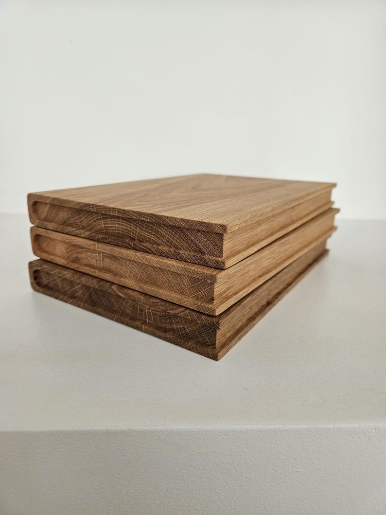 May include: Three stacked wooden blocks with a book-like appearance. The blocks are made of light brown wood, with visible grain patterns. The edges are slightly rounded, giving them a soft look. The blocks are stacked on top of each other.