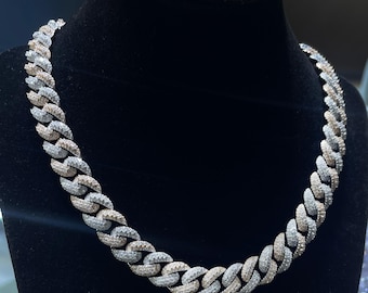 May include: A silver and rose gold chain necklace with a Cuban link design. The chain is fully iced out with clear and white diamonds.