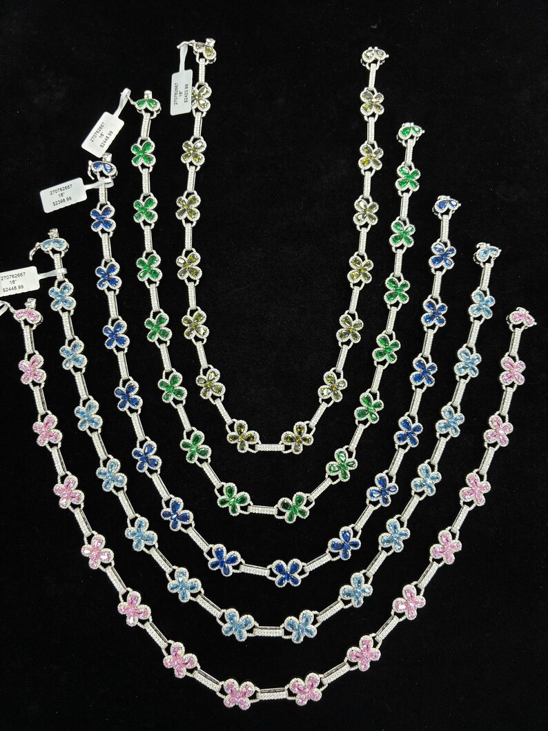 May include: A collection of silver necklaces with flower-shaped pendants in various colors, including pink, blue, and green. Each necklace is approximately 16 inches long, displayed against a black background.