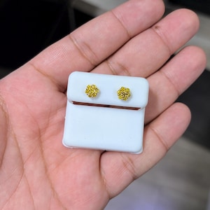以下が含まれることがあります： 小さくて丸い黄色のスタッドピアス。イヤリングはテクスチャード加工されたクラスターデザインで、白いイヤリングカードに表示されています。イヤリングはニュートラルな背景にあります。