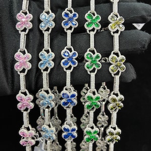 May include: A collection of silver bracelets, each featuring a floral design with various colored gemstones. The bracelets are adorned with pink, light blue, dark blue, green, and olive-green flower-shaped stones, and are connected by a line of small, clear stones.