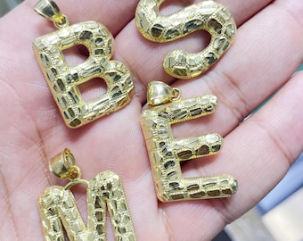 May include: Four gold-colored pendants in the shape of the letters B, E, M, and S. Each letter has a textured surface.