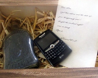 May include: A wooden box with a handwritten note, a glass bottle filled with black sand, and a black BlackBerry smartphone.