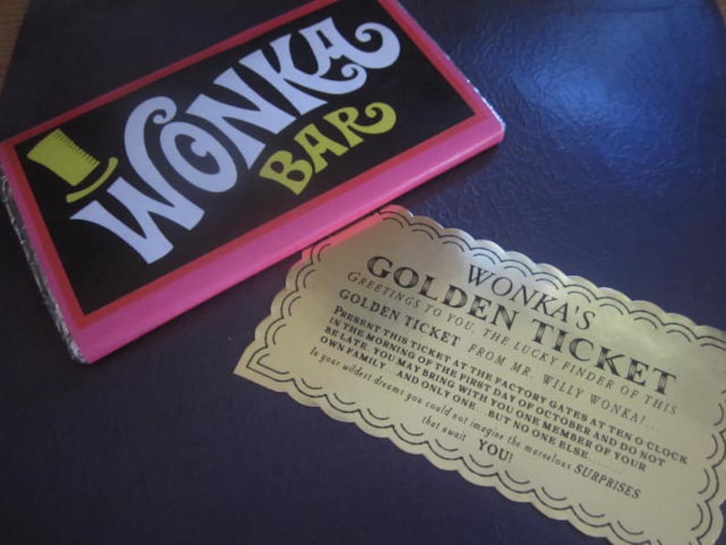 以下が含まれることがあります： 「Wonka's Golden Ticket」と書かれた金色のチケットと、10月1日の午前10時に工場の門でチケットを提示することについてのメッセージ。チケットは、ピンクと黒のWonkaバーのある濃い青色の表面の上に置かれています。