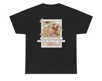 Puede incluir: Camiseta negra con un diseño de sello postal. El sello presenta el texto "GOD CREATED THE HEAVENS AND THE EARTH" e ilustraciones de manos, flores y mariposas. La camiseta tiene un cuello redondo clásico.