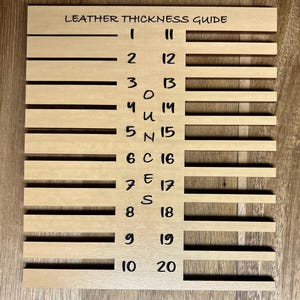 Puede incluir: Una guía de espesor de cuero de madera con el texto "LEATHER THICKNESS GUIDE". La guía tiene ranuras horizontales etiquetadas del 1 al 20. La madera es de color marrón claro. Medidas en milímetros.