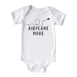 Puede incluir: Body de beb&eacute; blanco con mangas cortas. El body presenta el texto "AIRPLANE MODE" en negro, junto con una l&iacute;nea de puntos y un avi&oacute;n. Tiene cierres de presi&oacute;n en la parte inferior.