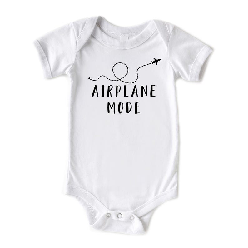 Puede incluir: Body de beb&eacute; blanco con mangas cortas. El body presenta el texto "AIRPLANE MODE" en negro, junto con una l&iacute;nea de puntos y un avi&oacute;n. Tiene cierres de presi&oacute;n en la parte inferior.