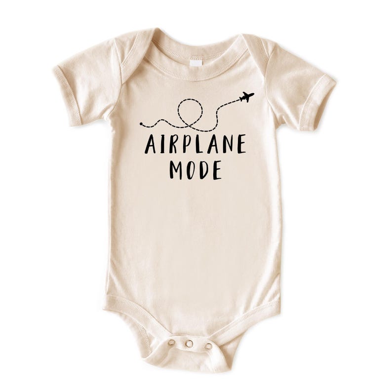 Puede incluir: Body de beb&eacute; color crema con mangas cortas. El texto negro "AIRPLANE MODE" est&aacute; impreso en la parte delantera, acompa&ntilde;ado de una l&iacute;nea de puntos y un peque&ntilde;o avi&oacute;n. El body tiene cierres de presi&oacute;n en la parte inferior.