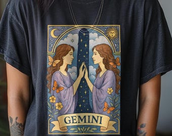 Puede incluir: Una camiseta negra con un diseño del signo zodiacal Géminis. El gráfico incluye dos mujeres mirándose, enmarcadas por un arco azul con una luna y un sol. La palabra "GEMINI" se muestra en una pancarta.