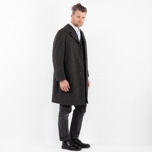 May include: A dark gray wool overcoat with a single-breasted closure and a notched collar. The coat has a textured pattern and is worn over a white button-down shirt.