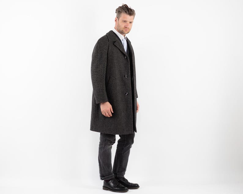 May include: A dark gray wool overcoat with a single-breasted closure and a notched collar. The coat has a textured pattern and is worn over a white button-down shirt.