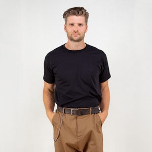 May include: A black crew neck t-shirt paired with brown pants and a brown belt. The belt has a silver chain attached. The person is standing in front of a white background.