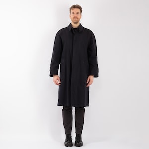 May include: A black long-sleeved coat with a button-up front and a collar. The coat is worn by a person standing in front of a white background.