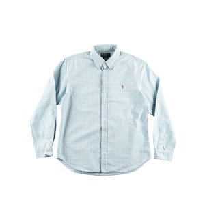 Può includere: Una camicia button-down a quadri azzurri e bianchi con maniche lunghe. La camicia ha un colletto button-down e un piccolo logo marrone sul petto. La camicia è realizzata in tessuto leggero.