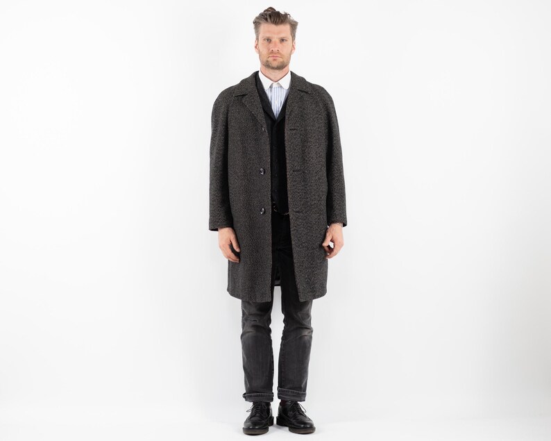 May include: A dark gray wool coat with a black button closure and a white collared shirt underneath.