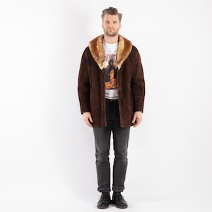 Puede incluir: Una chaqueta de ante marrón con cuello de piel sintética. La chaqueta tiene cierre de botones y dos bolsillos.