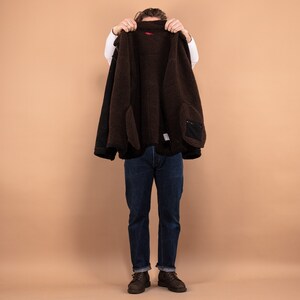 May include: A brown fleece-lined jacket with a black outer layer. The jacket is being held open by a person, revealing the fleece lining.