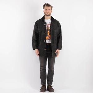 May include: A black corduroy jacket with a button-up front and a collar. The jacket has a slightly distressed look and is worn by a person with dark hair and a white t-shirt.