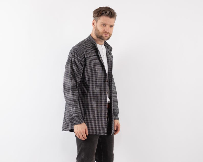 以下が含まれることがあります： 白と黒のチェック柄の長袖シャツに白いインナーを着た男性。シャツはボタンダウンカラーでゆったりとしたシルエットです。