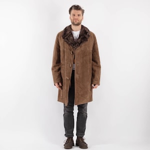 Puede incluir: Una chaqueta de ante marrón con cuello de piel marrón. La chaqueta tiene cierre de botones y dos bolsillos.