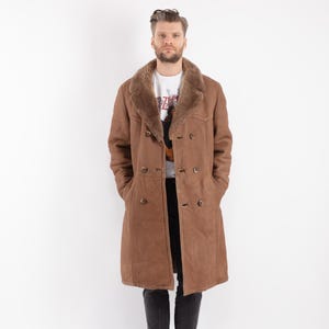 Puede incluir: Un abrigo de piel de oveja marrón con cuello de piel de oveja y cierre de doble botonadura. El abrigo es largo y está hecho de un material suave y lujoso.