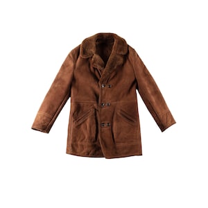 Puede incluir: Una chaqueta de ante marrón con un cuello y forro interior de piel sintética de color marrón oscuro. La chaqueta incluye mangas largas, dos bolsillos delanteros y un cierre frontal con tres botones visibles en el centro de la prenda.