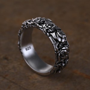 May include: A silver band ring with a detailed rose design. The ring is made of sterling silver and has a polished finish.