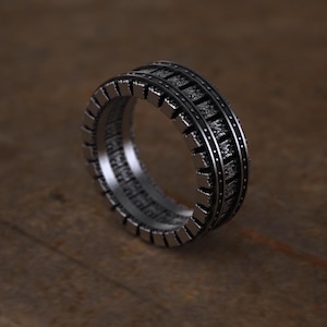 May include: A silver ring with a textured, geometric design. The ring has a wide band and a detailed pattern.