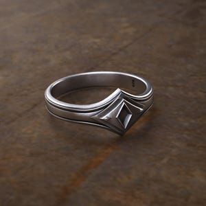 May include: A silver ring with a geometric design featuring a diamond-shaped center piece.