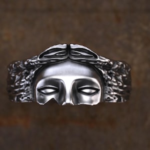 May include: A silver ring with a detailed design of a woman's face with a crown of leaves.