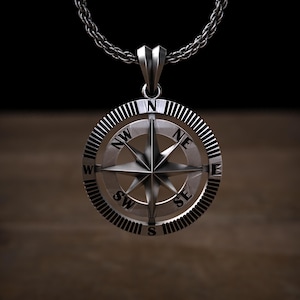 May include: Silver compass pendant necklace with a detailed compass design and black markings for the cardinal directions. The compass is on a silver chain.