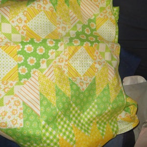 May include: A patchwork quilt with a yellow, green, and white color scheme. The quilt is made of various fabrics with different patterns, including stripes, polka dots, and floral designs.